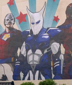 Chris Smith (John Cena) and Emilia Harcourt (Jennifer Holland) look up at a mural of the Top Trio in Peacemaker